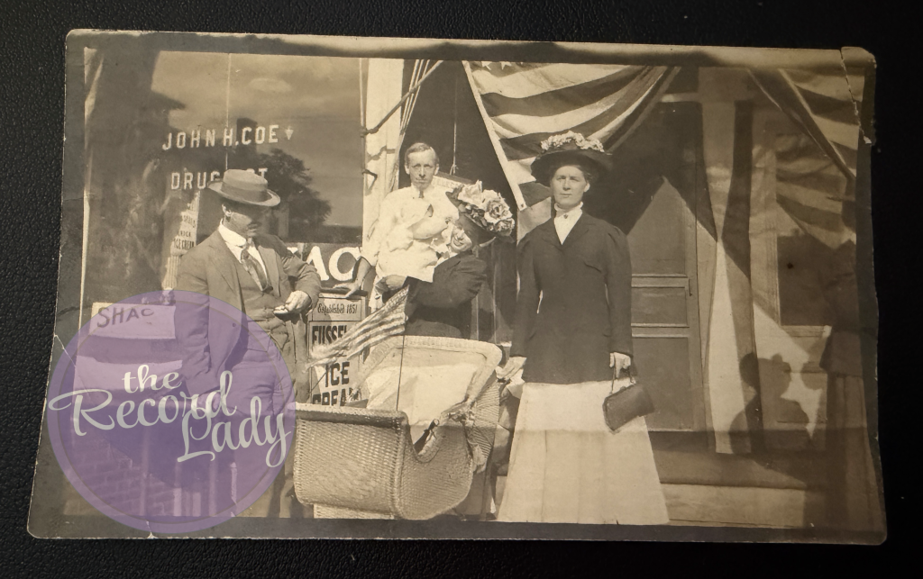 Early 1900s photograph of 4 people and a baby in front of drugstore